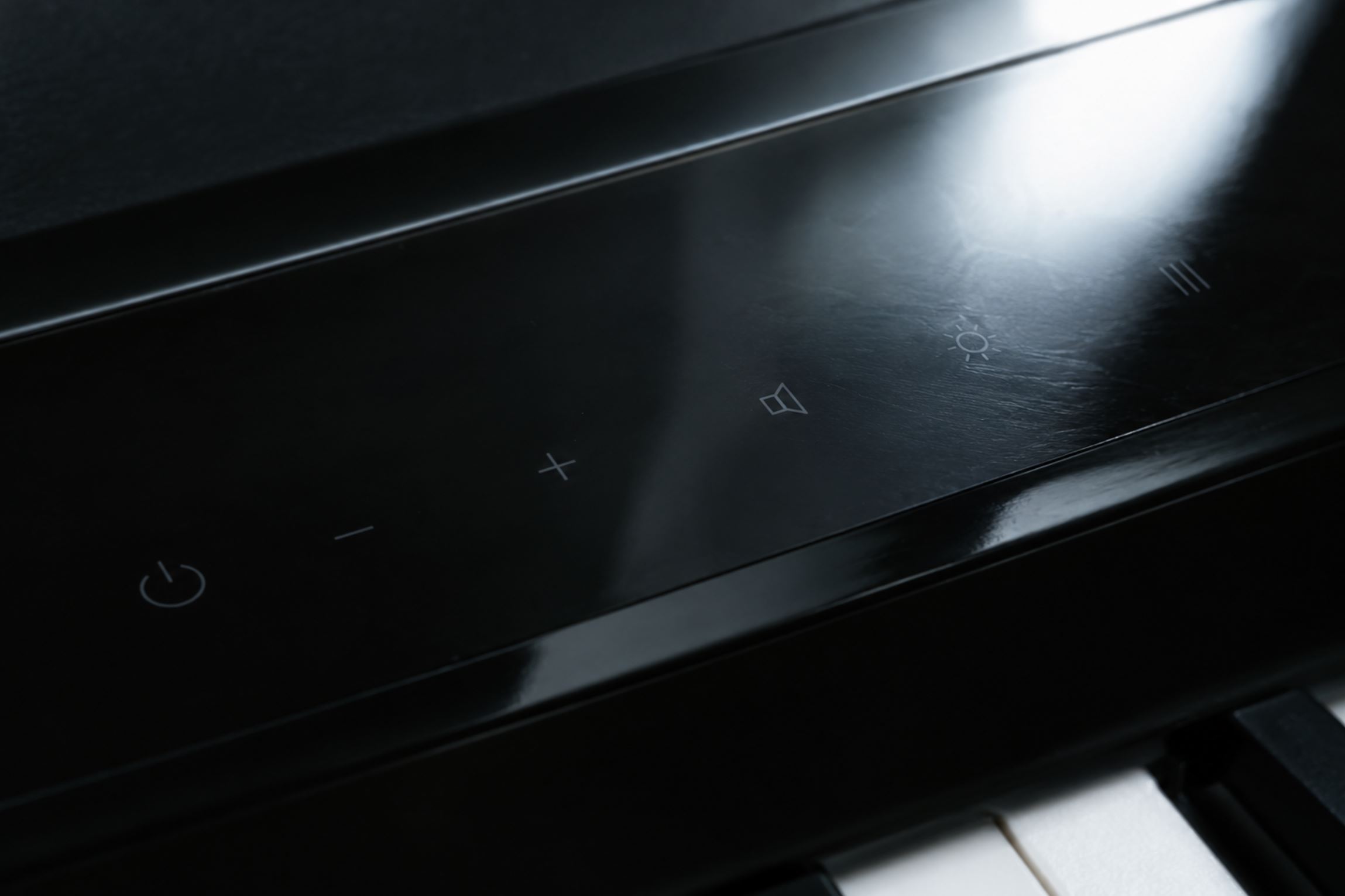 Macro close up of a flat glossy touch-sensor control panel on a modern instrument, faint printed icons barely visible against the dark reflective surface, hard overhead light creating glare across it, cold and sleek